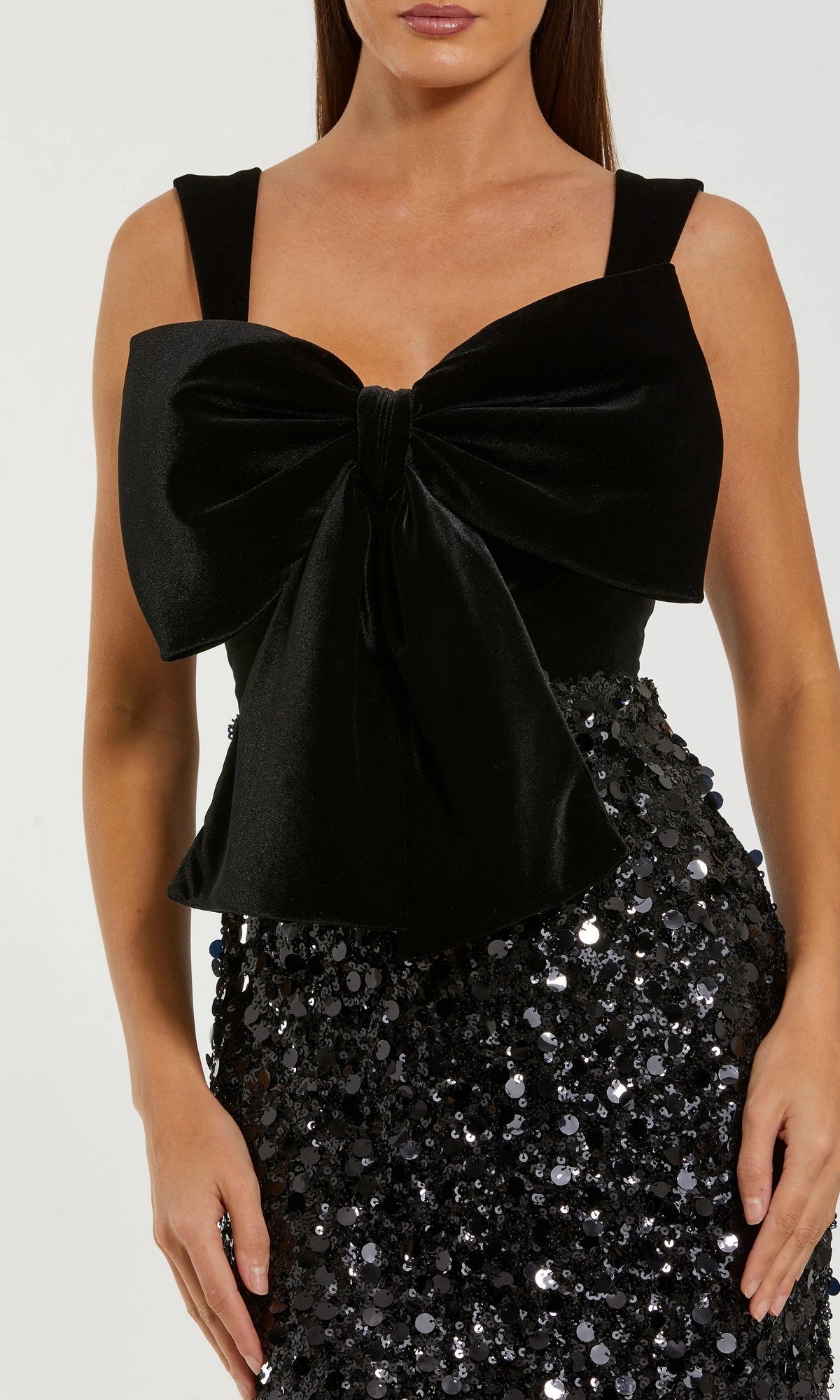 Woman wearing the Mac Duggal 27777 Midi Semi-Formal Dress featuring a sleeveless design, large velvet bow on the chest, and a sequined skirt for extra sparkle.